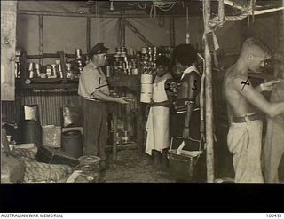 Yule Island, New Guinea. c. 1944-05-15. Lieutenant W. R. Burgess issues part of the day's ration to John the native cook at the Quartermasters Store at 1 Marine Food Supply Platoon. Left to right: ..