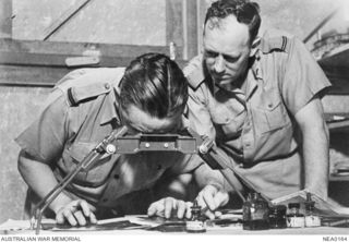 Two RAAF Intelligence Officers, 255538 Flying Officer (FO) Harold Peter Moschetti (left) and 255266 FO Stuart Patrick King, examine aerial photographs of the Japanese-held Kahili airstrip on ..