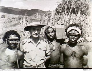 Garoka, New Guinea, 1945. Informal outdoors portrait of Wing Commander Arthur Howard RAAF, with native Papuan porters. The Papuans are wearing head and neck ornaments of various kinds, including ..