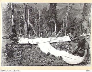 ULUNKOHOITU, YAMIL AREA, NEW GUINEA, 1945-07-18. PTE P.W. BOND (1), PTE E.J. GOUDIE (2) AND PTE G.E. CLARK (3), MEMBERS OF 8 PLATOON, A COMPANY, 2/6 INFANTRY BATTALION, LAYING PANEL STRIPS AS A ..