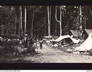 REINHOLD HIGHWAY, NEW GUINEA, 1943-08-31. NATIVE ROAD WORKERS DUE FOR LEAVE LINE UP OUTSIDE THE AUSTRALIAN AND NEW GUINEA ADMINISTRATION UNIT HEADQUARTERS FOR THEIR LEAVE PASSES
