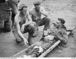 BOUGAINVILLE. 1945-05-21. CORPORAL G.T. MILLS (1) AND PRIVATE R.A. WHITE (2), MEMBERS OF D COMPANY, 58/59 INFANTRY BATTALION, CHATTING TO A FRIEND ABOUT THE ACTION WHILE AWAITING JEEP AMBULANCE ..