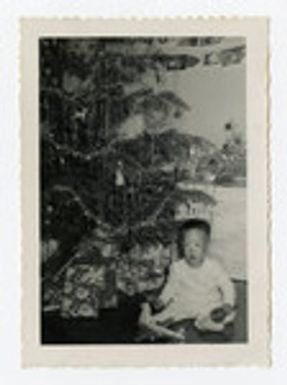 Young boy sitting next to Christmas tree