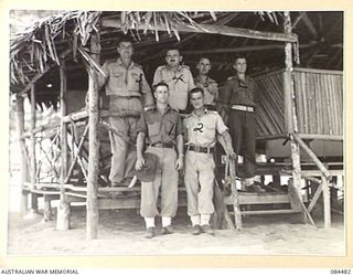LAE, NEW GUINEA. 1944-12-18. OFFICERS GATHERED IN THE ENTRANCE OF THE OFFICERS' MESS, 12 SMALL SHIP COY. IDENTIFIED PERSONNEL ARE:- LIEUTENANT D B HOPE, (1); LT J J YOUNG, (2); MAJOR J H TURNER, ..