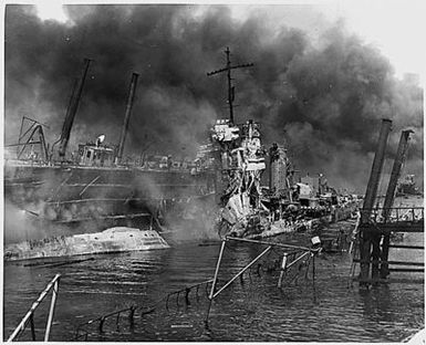 Naval photograph documenting the Japanese attack on Pearl Harbor, Hawaii which initiated US participation in World War II. Navy's caption: The twisted remains of the destroyer USS SHAW burning in floating drydock at Pearl Harbor after the "sneak Japanese attack" on Dec. 7, 1941.