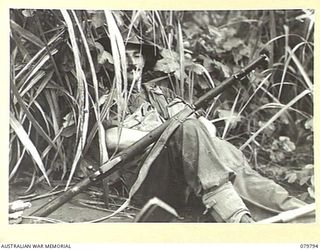 BUT AREA, NEW GUINEA. 1945-03-17. NX4367 CORPORAL E.L. MCCARTNEY, C. COMPANY, 2/2ND INFANTRY BATTALION, TAKING A WELL EARNED REST IN THE KUNAI GRASS BEFORE CROSSING THE NINAHAU RIVER