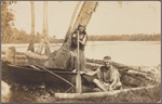 Couple posed with outrigger canoe beneath palm tree, lagoon in background.