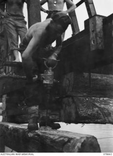 MOTUPENA POINT, BOUGAINVILLE ISLAND, 1945-01-26. NX162279 CORPORAL D.P. COOPER, 23RD FIELD COMPANY, USING A COMPRESSED AIR DRILLING MACHINE DURING THE BUILDING OF A WOODEN PILE BRIDGE ACROSS THE ..