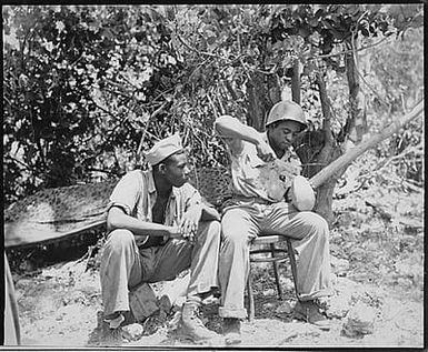 "Marine Sgt. F. Smit...and Cpl. S. Brown...open a coconut to get a cool drink on Saipan."