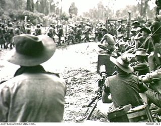 THE SOLOMON ISLANDS, 1945-09-19. AUSTRALIAN SERVICEMEN, INCLUDING A MACHINE GUNNER, WATCH JAPANESE TROOPS FROM NAURU ISLAND ENTERING AN INTERNMENT CAMP ON BOUGAINVILLE ISLAND AFTER MARCHING FROM ..