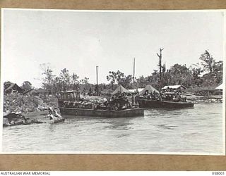 LAE, NEW GUINEA, 1943-10-12. TWO LANDING BARGES LADEN WITH TROOPS AND EQUIPMENT PULLING IN TO THE DOCKS