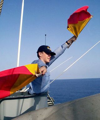 Signalman Scott K. Gliebe uses semaphores aboard USS GUAM (LPH 9) to signal other ships nearby. GUAM is deployed to the Persian Gulf in support of Operation Southern Watch