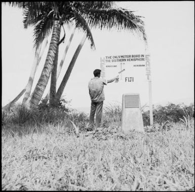 Man standing at a sign indicating where the International Date Line crosses Taveuni Island, Fiji, 1966 / Michael Terry
