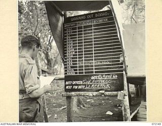 KILIGIA, NEW GUINEA. 1944-04-08. NX137071 LIEUTENANT R.S. MCGOVERN AT HEADQUARTERS 5TH DIVISION CHECKING THE "WARNING OUT BOARD" WHICH INDICATES THE LOCATION OF STAFF OFFICERS