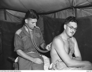 RABAUL, NEW BRITAIN. 1945-11-09. MAJOR G.M. BLAXLAND, MEDICAL OFFICER, 105 CASUALTY CLEARING STATION (1) RUNNING A STETHOSCOPE OVER CAPTAIN W.J. STONEY (2) DURING A DEMOBILISATION MEDICAL ..