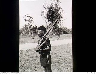 Madang, New Guinea, c. 1944-12-25. Near Headquarters, RAAF Northern Command (NORCOM), Sergeant (Sgt) Kimari of the Royal Papuan Constabulary (RPC) stands at attention during a traditional dance ..