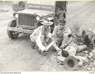 LAE, NEW GUINEA. 1944-09-21. A MEMBER OF THE NEW GUINEA FORCE PROVOST COMPANY, SERGEANT H.H. BURNISTON (1) RENDERING FIRST AID TO AN INJURED DESPATCH RIDER, CORPORAL L. BYRNE (3). IDENTIFIED ..