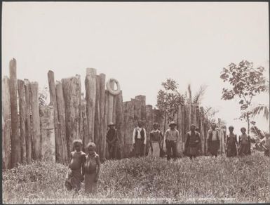 Villagers standing next to the outside palisade of Nore Fou, Solomon Islands, 1906 / J.W. Beattie