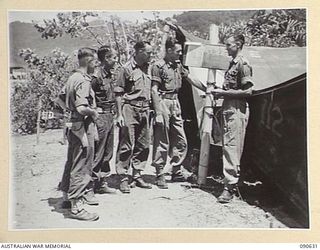 BUT, NEW GUINEA. 1945-04-10. D COMPANY, 2/8 INFANTRY BATTALION OFFICERS EXAMINING A MAP ON A NOTICE BOARD OUTSIDE COMPANY HQ. IDENTIFIED PERSONNEL ARE:- LT G.T. BEHAN (1); CAPT R.J. MCDERMOTT (2); ..