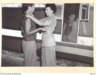 LAE, NEW GUINEA. 1945-11-23. CORPORAL M. READER BEING FITTED FOR A BLOUSE BY THE INSTRUCTOR, SERGEANT E. HUMBERG, DURING THE DRESSMAKING CLASS HELD AT THE LAEWAS COLLEGE, AWAS BARRACKS, LAE