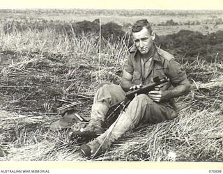 RAMU VALLEY, NEW GUINEA, 1944-02-29. QX34295 PRIVATE E. RYAN, A MEMBER OF THE MORTAR PLATOON, 2/12TH INFANTRY BATTALION, CLEANING HIS OWEN GUN WHILST RESTING AT KESAWAI