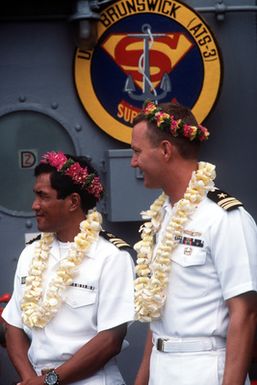 LCDR Spencer R. King, right, Commanding Officer of the salvage and rescue ship USS BRUNSWICK (ATS-3), and another officer wear garlands and leis presented to them after the ship's arrival at Majuro Atoll. The BRUNSWICK will be in the islands for 90 days while its crew salvages a wreck that is blocking the harbor at the island of Jaluit