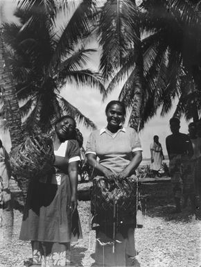 [Portrait of two Pacific Island women holding woven baskets]