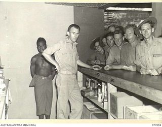 LAE AREA, NEW GUINEA. 1944-11-26. NX192921 PRIVATE V.W. CONNOLLLY AND HIS AUSTRALIAN NEW GUINEA ADMINISTRATIVE UNIT NATIVE ASSISTANTS SERVING CUSTOMERS AT THE CANTEEN OF THE 22ND ARMY CANTEEN ..