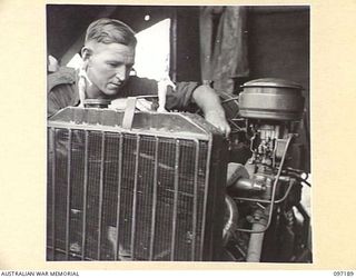 CAPE WOM, NEW GUINEA. 1945-09-27. PRIVATE A.K. BOYD, 110 BRIGADE ORDNANCE FIELD PARK, INSPECTING THE MOTOR WHICH POWERS THE UNIT LIGHTING PLANT