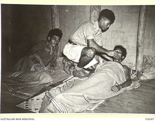 NEW GUINEA. 1942-08. A PAPUAN NATIVE MEDICAL ORDERLY ATTENDS TO A SICK NATIVE IN ONE OF THE WARDS OF THE HOSPITAL OPERATED BY THE NATIVE MEDICAL SERVICES. THESE NATIVE ORDERLIES HAVE RECEIVED ..