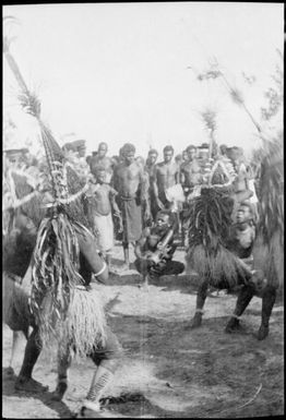 Four dancers wearing tall and narrow headdress with many onlookers, New Guinea, ca. 1929 / Sarah Chinnery