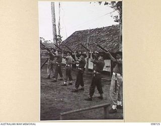 DALLMAN HARBOUR, NEW GUINEA. 1945-11-11. MEMBERS OF 2/5 INFANTRY BATTALION SALUTE THEIR FALLEN COMRADES WITH THREE VOLLEYS OF RIFLE FIRE DURING A MEMORIAL SERVICE HELD IN THE UNIT LINES IN HONOUR ..