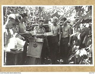 FINSCHHAFEN, NEW GUINEA. 1943-12-24. QX8995 STAFF SERGEANT A. IRVINE (1) OF HEADQUARTERS 9TH DIVISION, ISSUING THE AUSTRALIAN COMFORTS FUND CHRISTMAS HAMPERS TO TRANSPORT DRIVERS OF THE 9TH ..