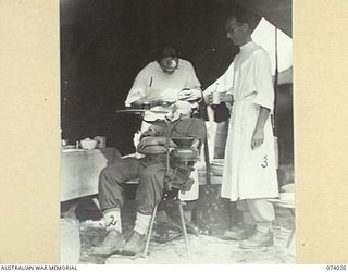 SIAR PLANTATION, NEW GUINEA. 1944-06-18. NX146381 CAPTAIN H. BEVAN, DENTAL OFFICER, FILLING A TOOTH FOR V48135 SERGEANT C. WALTERS (2); ASSISTED BY TX10813 PRIVATE W.C. CAWSE (3) IN THE TENT ..