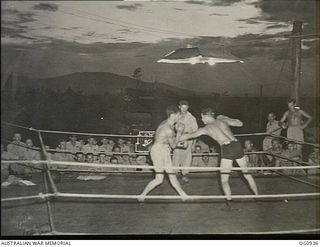 NADZAB, NEW GUINEA. C. 1944-02. RAAF MEMBERS OUTDOORS WATCHING AT NIGHT UNDER LIGHTS BOXING IN THE PAT CRAIG STADIUM, NAMED AFTER "ADOPTED" TIVOLI GIRL PERFORMER. THE CONTESTANTS ARE LEADING ..