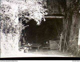 Rabaul, New Britain, 1945-10. The entrance to a large tunnel or cave where Japanese soldiers hid themselves and their equipment. Inside the tunnel are several beds or stretchers, on one of which an ..