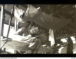 Salamaua, New Guinea. 1943-09-20. V75540 Corporal S.C. Mulhall, 11th Field Company, Royal Australian Engineers, sitting in his bunk writes home from his new home on the isthmus. Note the occupied ..