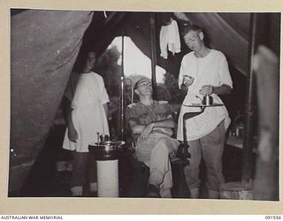 SORAKEN AREA, BOUGAINVILLE. 1945-04-03. CAPTAIN H. AKEROYD, THE DENTIST AT 19 FIELD AMBULANCE (1), ATTENDING TO THE TEETH OF LIEUTENANT G.I. HEILBRONN (2)