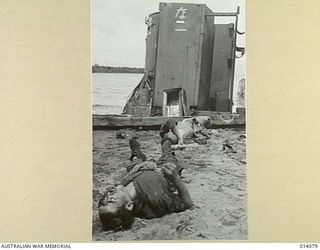 1943-01-14. PAPUA. SMASHED JAPANESE LANDING BARGE AND DEAD JAPANESE LITTER THE BEACH AT BUNA. (NEGATIVE BY BOTTOMLEY)