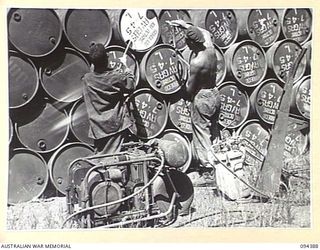 LAE AREA, NEW GUINEA. 1945-07-12. CORPORAL H.C. MARSHALL, 2 BULK PETROLEUM STORAGE COMPANY, OPERATING THE STENCILLING PLANT TO MARK DRUMS. THREE THOUSAND 44-GALLON DRUMS ARE TURNED OUT DAILY BY THE ..