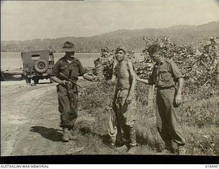 Wewak Area, New Guinea. April 1945. A member of the Australian 6th Division 2nd AIF escorts a Japanese prisoner to a jeep near Wewak while his partner, with the machine gun, remains on the alert