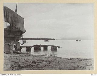 WIDE BAY, NEW BRITAIN, 1945-05-02. THE JETTY AT GOLDEN BEACH WITH NO 41 LANDING CRAFT COMPANY BARGES IN THE BAY. TOL PLANTATION LIES AT THE LEFT AND THE SOUTHERN TIP OF THE WIDE BAY HEADLAND LIES ..