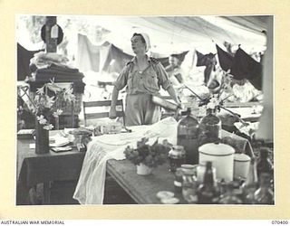 FINSCHHAFEN, NEW GUINEA, 1944-01-31. VFX59385 SISTER L. RAE AT HER TABLE IN WARD 6 OF THE 2/3RD CASUALTY CLEARING STATION. THE FLOWERS IN THE SHELL CASES ARE BROUGHT BY NEW GUINEA NATIVES TO ..