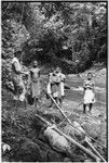 Carriers and Pete Vayda with cargo tied to poles beside a river