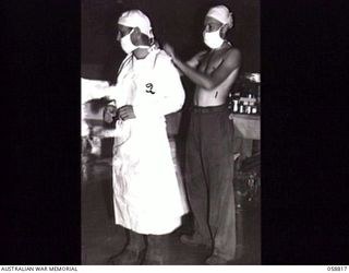 DUMPU, NEW GUINEA. 1943-10-15. MEDICAL ORDERLY QX42621 PRIVATE S. V. DOW OF THE 2/6TH AUSTRALIAN FIELD AMBULANCE WITH "E" SURGICAL TEAM, ADJUSTING THE OPERATING COAT OF THE SURGEON PRIOR TO AN ..