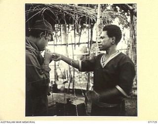 WASU, PAPUA, 1944-03-25. A MEMBER OF THE ROYAL PAPUAN CONSTABULARY GIVES A LIGHT THROUGH THE WIRE OF THE PRISONER OF WAR COMPOUND TO A JAPANESE PRISONER