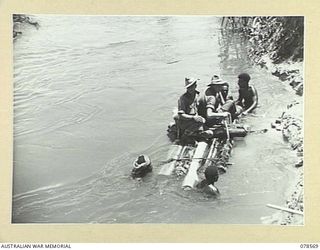 BOUGAINVILLE AREA. 1945-01-22. NATIVES TRANSPORTING AUSTRALIAN TROOPS ACROSS THE JABA RIVER ON A RAFT BUILT OF BANANA PALM LOGS