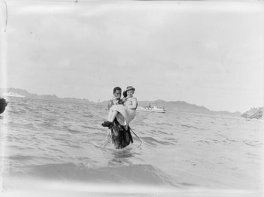 [Pacific Island man carries woman through water]
