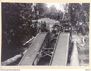 SOUTH BOUGAINVILLE. 1945-07-20. A COVENANTER BRIDGE BUILDING TANK OF 2/4 ARMOURED REGIMENT, LAYING A 32-FOOT SPAN OVER A ROAD WASH-AWAY BETWEEN THE OGORATA AND MOBIAI RIVERS TO ALLOW URGENTLY ..