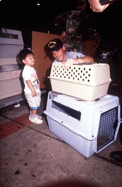 A sailor helps a young evacuee check on one of hundreds of pets arriving through customs during the evacuation of thousands of military and civilian personnel from the Philippine Islands. The evacuation, part of Operation Fiery Vigil, is the result of the June 10 eruption of Mount Pinatubo, which deposited more than four inches of volcanic ash on the Islands, disrupting base operations